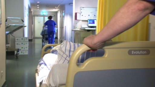 Eine Pflegeperson schiebt ein Krankenhausbett.