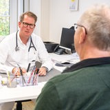 Ein Hausarzt stellt einem älteren Patienten eine Bescheinigung aus