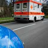 Ein Krankenwagen steht auf der Straße und die Haube eines Streifenwagens der Polizei ist unten links zu sehen.