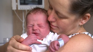Ein Neugeborenes liegt in den Armen seiner Mutter