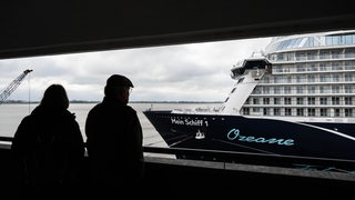 Zwei Menschen schauen auf ein Kreuzfahrtschiff auf der Columbuskaje in Bremerhaven.