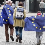 Eine Familie mit 2 Kindern läuft mit Europaflaggen auf der Straße.