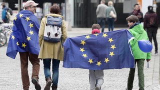 Eine Familie mit 2 Kindern läuft mit Europaflaggen auf der Straße.