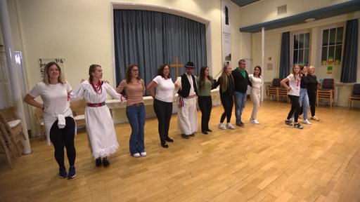Eine Reihe von Menschen tanzt in einem Gemeindehaus kroatische Volkstänze.