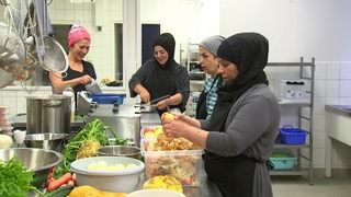 Vier Frauen mit Kopftuch arbeiten in einer Kantinenküche.