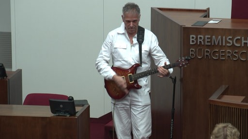 Ein Künstler in weiß gekleidet spielt Gitarre in der Bremer Bürgerschaft.