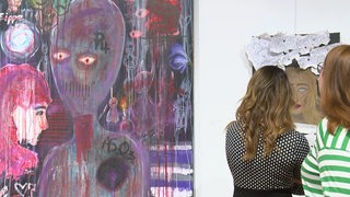 Zwei Studierende gucken sich ihre Kunstportaits in der Kunstausstellung Who I am an. 