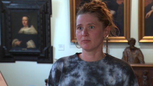 Künstlerin Helena Otto im Interview. Hinter ihr sind Gemälde zu sehen.