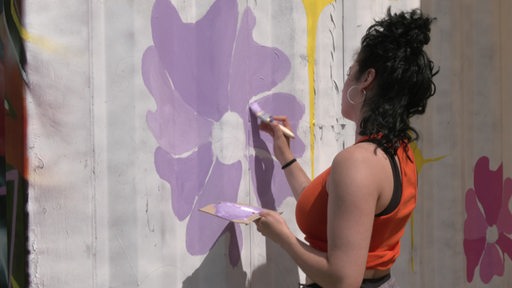Eine Künstlerin malt eine lilane Blume.