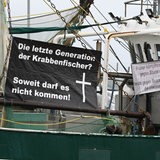 An einem Kutter hängt ein Plakat mit der Aufschrift "Die letzte Generation der Krabbenfischer?" Soweit darf es nicht kommen!".