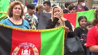 Zwei Frauen auf der bremer Kundgebung die eine Afghanistan Flagge in der Hand halten. Die eine Frau weint und verdeckt mit einem Kopftuch ihr Gesicht.