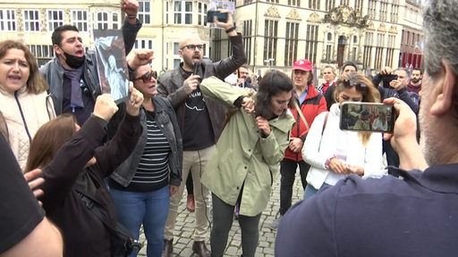 Die Studentin Nazanin Asadi schneidet mit einer Schere ihre Haare ab umgeben von Demonstranten in Bremen. 