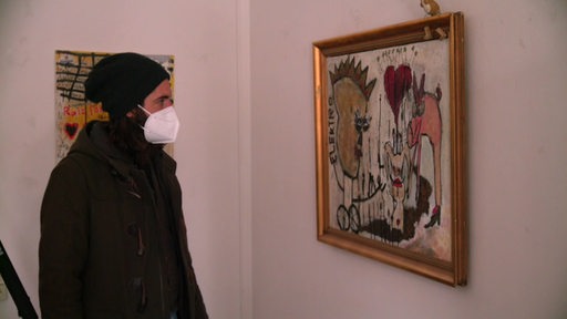 Freddy Radeke mit Mütze und Mundschutz vor einem Gemälde-