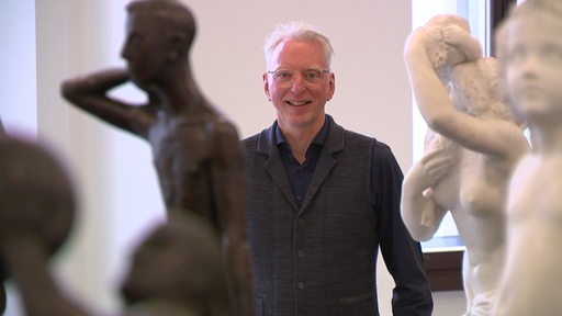 Der Stammgast Peter Brockmann steht hinter Staturen in der Bremer Kunsthalle.
