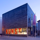 Blick auf ein kastenförmiges Backsteingebäude. Im Fenster steht in großen Lettern "KUNST".