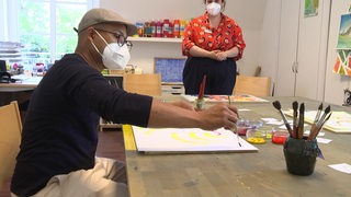 Ein Patient malt ein Bild mit der Beaufsichtigung einer Therapeutin mit Wasser-Farben.