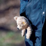 Ein Teddybaer ragt aus der Manteltasche einer Frau