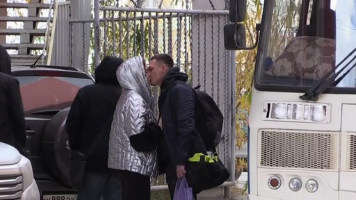 Ein Pärchen verabschiedet sich mit einem Kuss an einer Bushaltestelle.