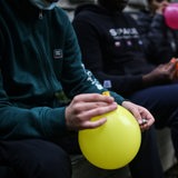 Junge Menschen sitzen mit Luftballons und Kartuschen auf einer Mauer und konsumieren Lachgas.