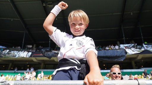 Ein kleiner Junge im deutschen Nationaltrikot strahlt kess von der Tribüne im Weser-Stadion aus in die Kamera.