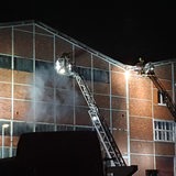 Feuerwehrleute stehen auf einer Drehleiter und löschen eine Lagerhalle. 
