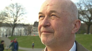Ein Mann blickt mit leicht zugekniffenen Augen zur Seite und hoch