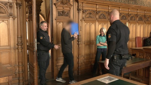 Ein Angeklagter wird von Polizisten in den Gerichtssaal des Bremer Landesgerichtes geführt.