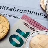 Auf einem Papier mit der Aufschrift "Gehaltsabrechnung" liegen Geldmünzen und eine Euro-Banknote.