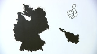 Eine Schwarz-Weiße Landkarte von Deutschland und von Bremen mit einer karikaturisierten hand mit Daumen nach oben.
