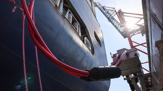 Die Landstromkabel eines Containerschiffs sind mit einer verfahrbahren Steckdose entlang dem Kai verbunden.