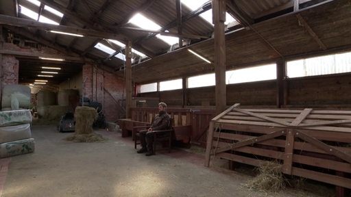 Landwirt Axel Duensing sitzt auf einer Bank in seiner Scheune.