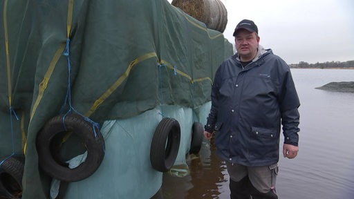 Ein Landwirt knietief im Wasser, neben ihm Strohballen.