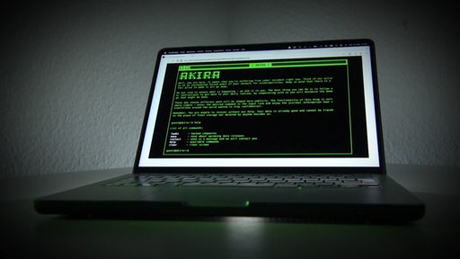 Ein Laptop steht in einem dunklen Raum, auf dem Bildschirm ist grüne Schrift vor einem schwarzem Hintergrund zu sehen