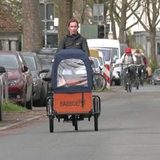 Eine Frau fährt auf einem Lastenrad die Straße entlang.