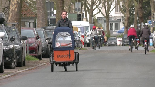 Eine Frau fährt auf einem Lastenrad die Straße entlang.