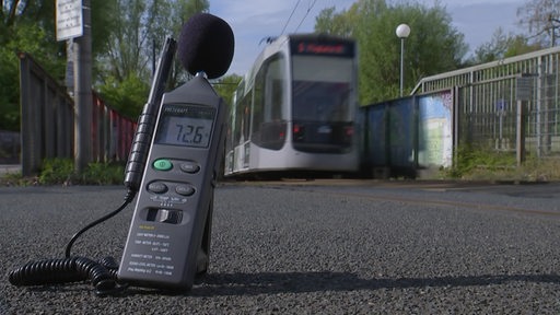 Im Vordergrund ist ein Lautsstärkemesser zu sehen und im Hintergrund fährt eine Straßenbahn entlang.
