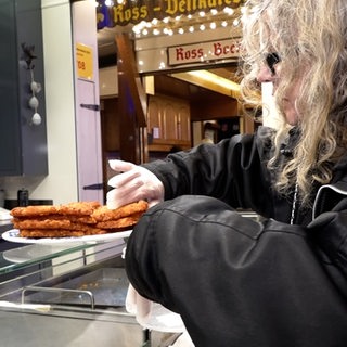 Eine Frau steht an einem Stand und packt Kartoffelpuffer ein.