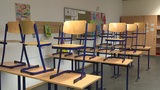 Ein leerer Klassenraum, in dem die Stühle auf den Tischen stehen.