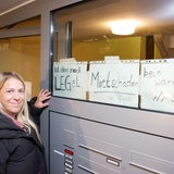 Blonde Frau präsentiert Aushängen zu "Mietschäden" vor Hauseingang