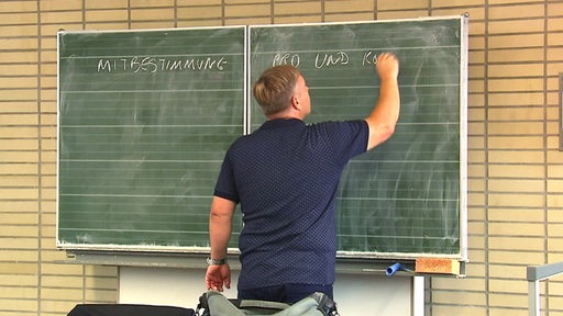 Ein Lehrer schreibt mit Kreide an eine Tafel in einer Schule.