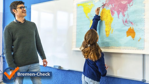 Ein lächelnder Lehrer beobachtet einen Grundschüler, der im Geografieunterricht auf eine Weltkarte zeigt
