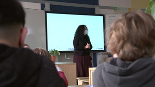 Eine Lehrerin steht vor einem Whiteboard vor ihren Schüler*Innen.