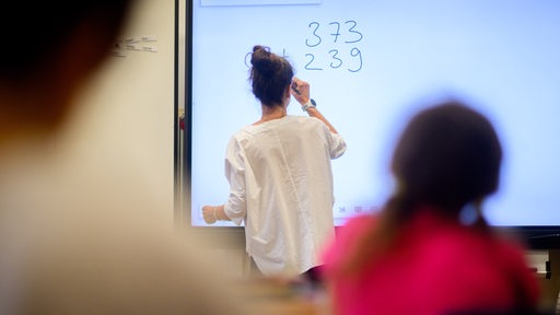 Ein Lehrerin schreibt eine Mathematikaufgabe an eine digitale Schultafel.