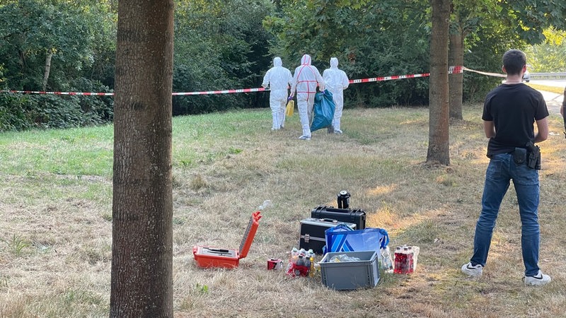 Polizisten in weißen Schutzanzügen tragen einen blauben Müllsack.