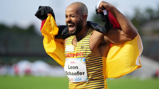 Leon Schäfer jubelt nach einem 100-Meter-Sprint mit einer Deutschland-Flagge.
