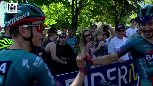 Links ist der Radprofi Lennard Kämner zu sehen, welcher einem anderen Radsportler die Hand schüttelt.