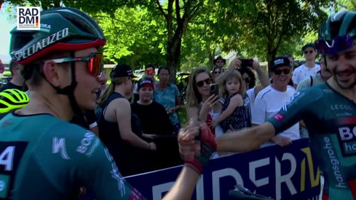 Links ist der Radprofi Lennard Kämner zu sehen, welcher einem anderen Radsportler die Hand schüttelt.
