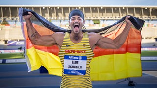 Leon Schäfer feiert mit einer Deutschlandfahne hinter seinem Rücken den WM-Sieg im Weitsprung