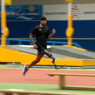 Ein Sportler mit Beinprothese läuft in einer Sporthalle.