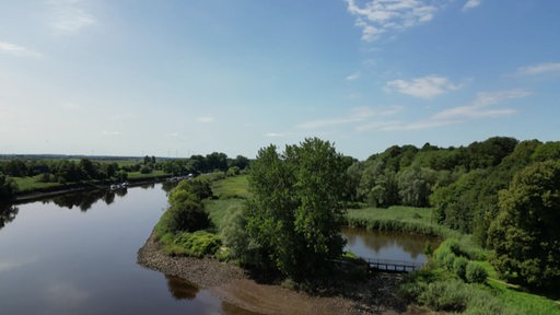 Bild eines Steinwehres, hinter dem ein kleiner See neben einem Fluss liegt. 